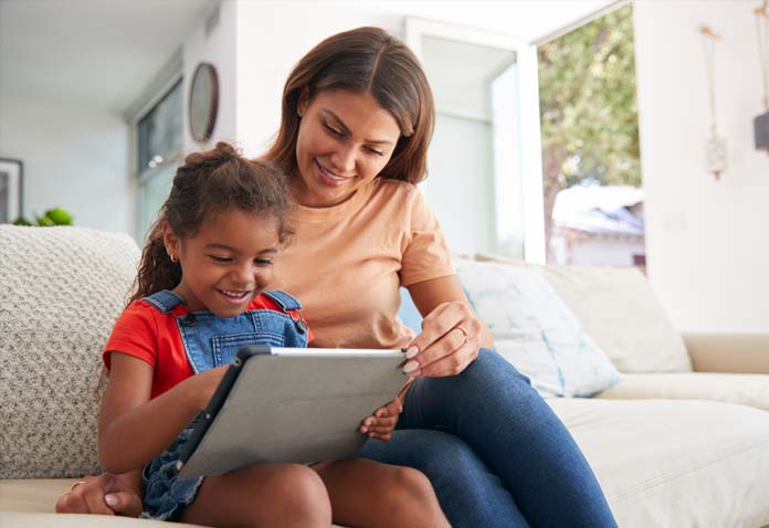 Woman and child sitting on a couch smiling while using a tablet