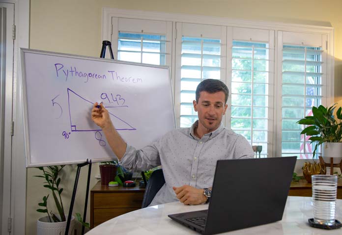 Man pointing to a graphic on a white board while looking at a laptop