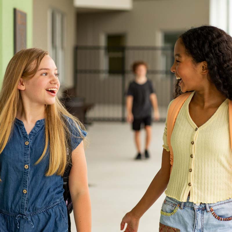 Two girls wearing backpacks and smiling at each other